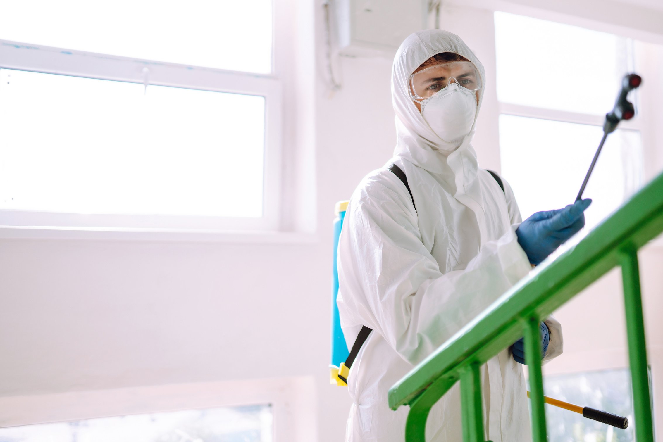 Man in Hazmat suit, protective gloves and goggles use sprayer equipment disinfect the entrance.